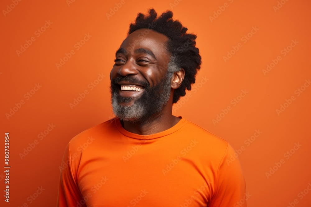 Obraz premium Portrait of a smiling afro-american man in his 50s showing off a lightweight base layer on soft orange background