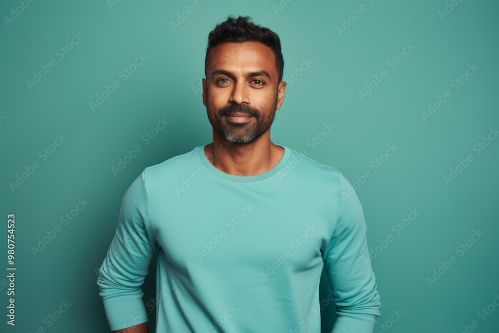 Portrait of a satisfied indian man in his 30s sporting a long-sleeved thermal undershirt over soft teal background Portrait of a satisfied indian man in his 30s sporting a long-sleeved thermal undershirt over soft teal background