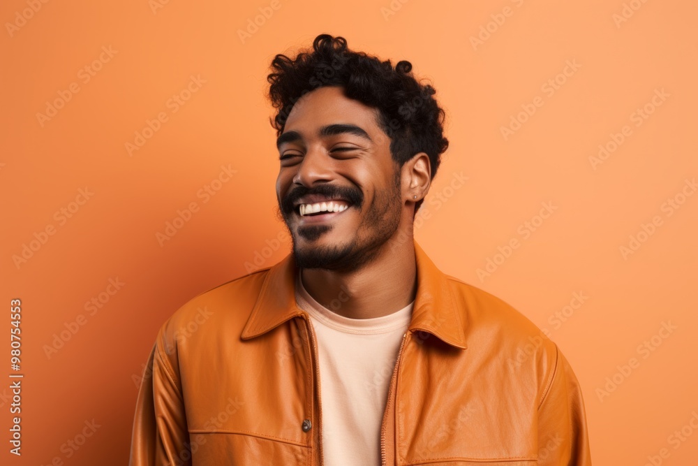 Portrait of a smiling indian man in his 20s wearing a trendy bomber jacket in soft orange background Portrait of a smiling indian man in his 20s wearing a trendy bomber jacket in soft orange background