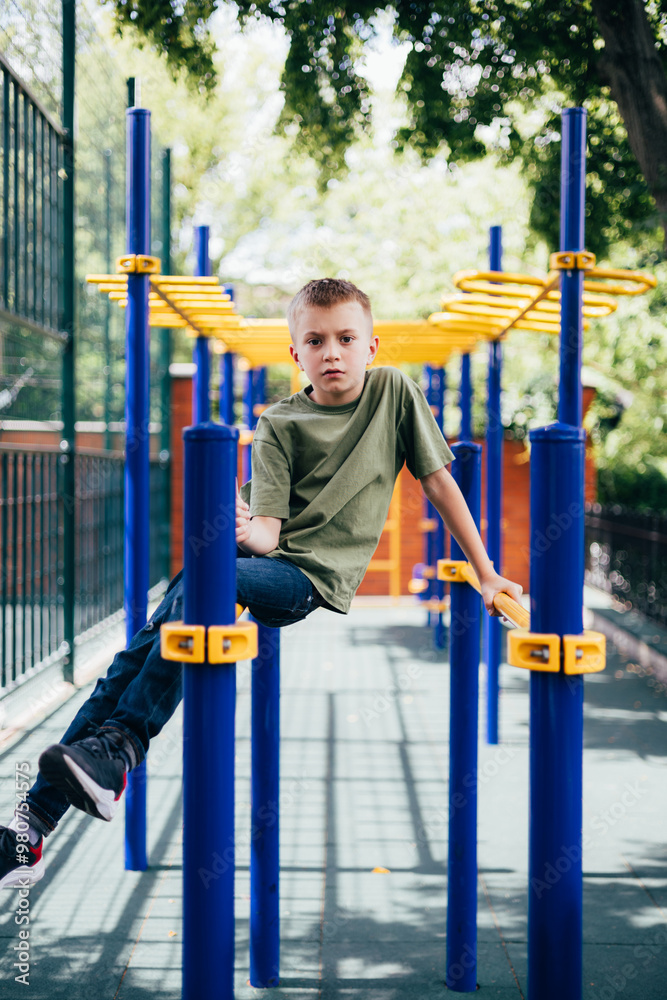 A school-age boy in a green T-shirt spends time on horizontal bars, a playground in sunny weather. Front view A school-age boy in a green T-shirt spends time on horizontal bars, a playground in sunny weather. Front view