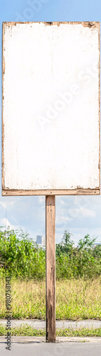 A white sign is standing in a field. The sign is empty and has a wooden post photo