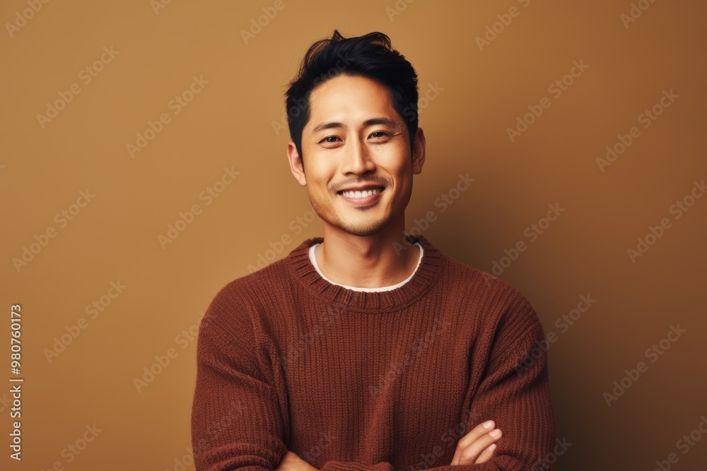 Fototapeta premium Portrait of a content asian man in his 30s wearing a cozy sweater in soft brown background