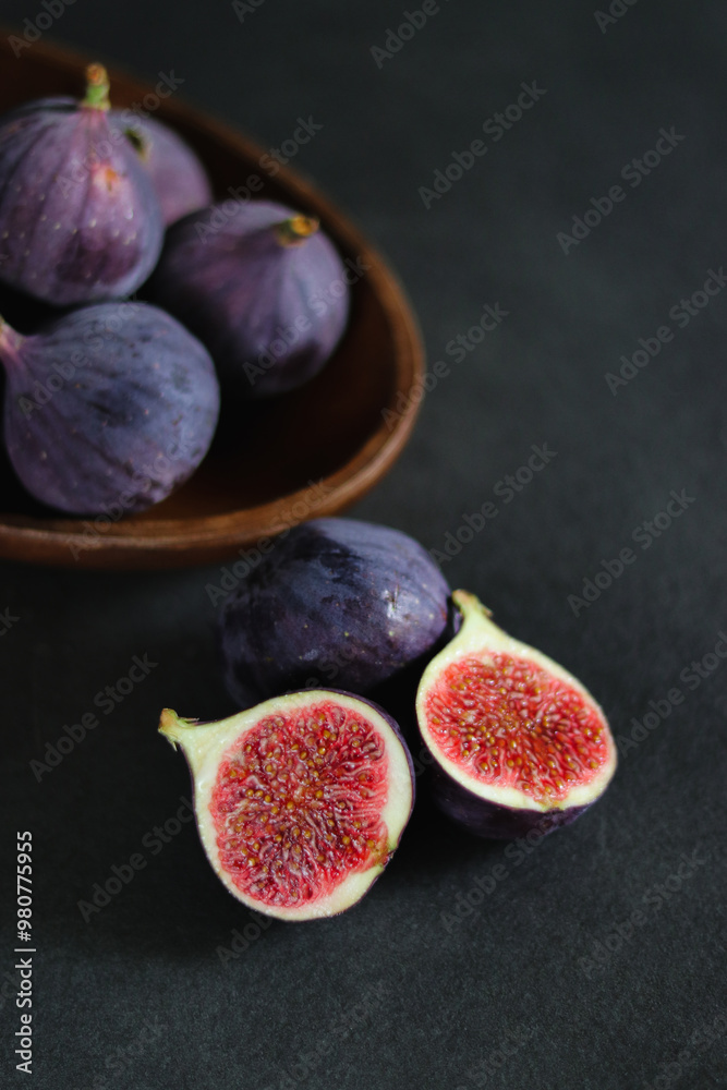 Close up of fresh ripe fig fruits in a wooden bowl on dark grey table Close up of fresh ripe fig fruits in a wooden bowl on dark grey table