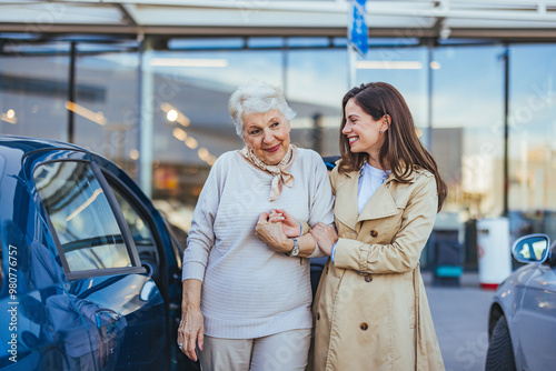 Young Woman Assisting Elderly Woman Near Car in Urban Setting photo