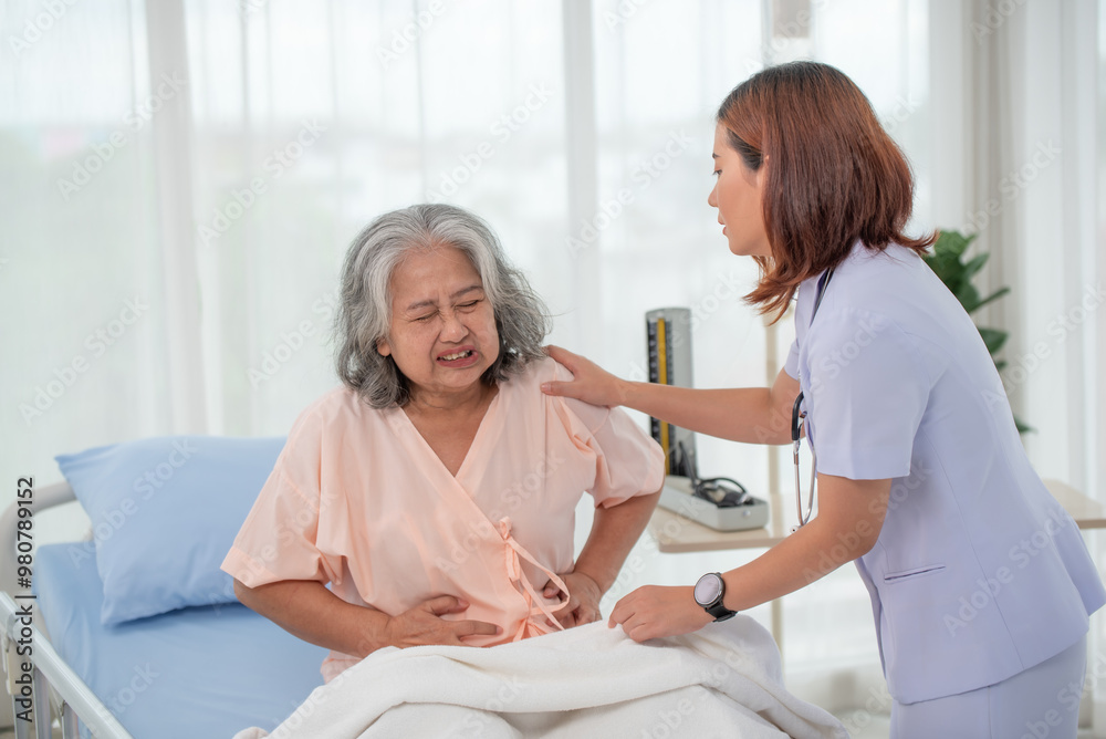 Asian nurse helping a senior Asian female patient with stomach ache on a bed in hospital Asian nurse helping a senior Asian female patient with stomach ache on a bed in hospital