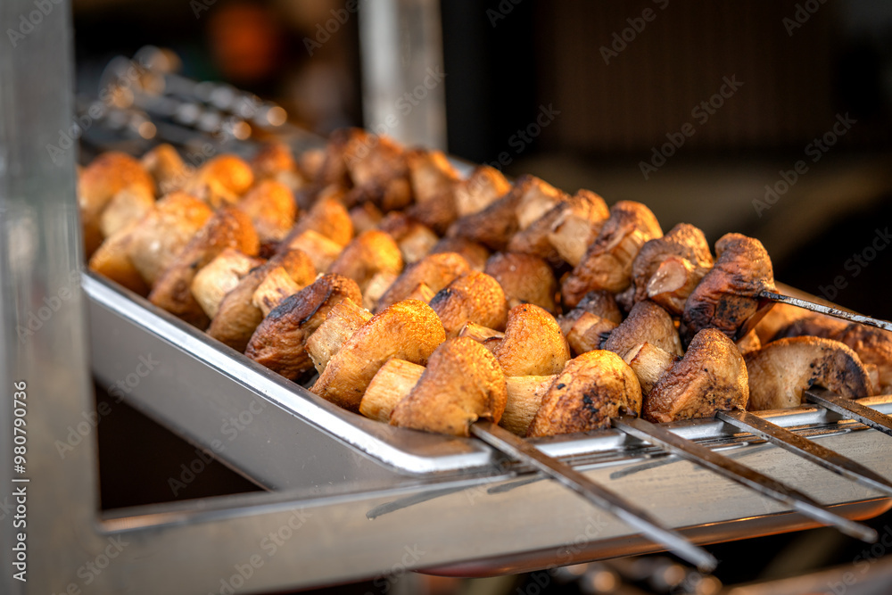 Mushrooms kebab (shish kebab) in close-up. Champignons fried on fire (barbecue) on skewers on the market counter. Delicious and mouth-watering vegan shashlik