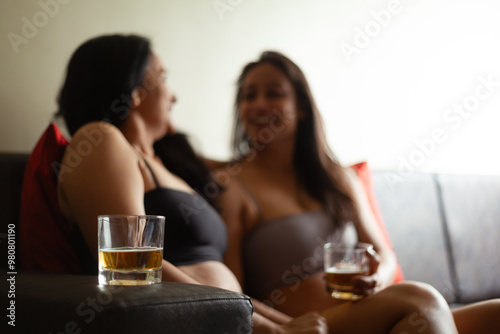 Two Indian women are happily talking and drinking cold beverages, sharing a cheerful moment together.