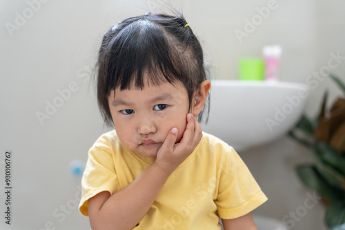 little asian girl presses hand to cheek, suffers from pain in tooth. Teeth decay, dental problems, child emotions and facial expression, oral health care, reducing sweets, fluorine coating