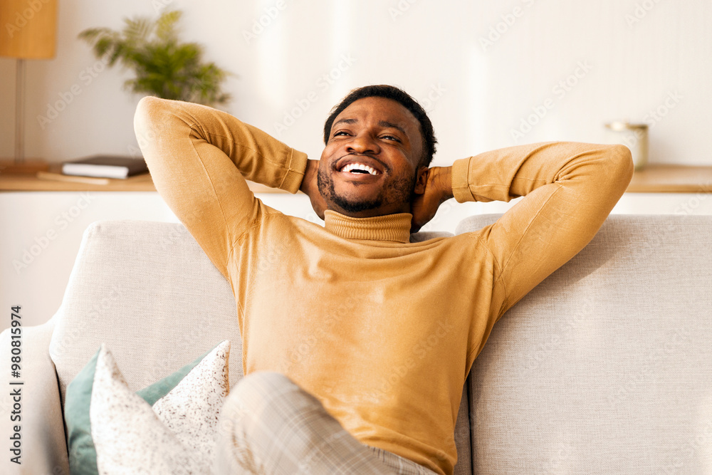 Weekend At Home. Happy Afro Man Relaxing Sitting On Sofa Holding Hands Behind Head Indoor. Copy Space Weekend At Home. Happy Afro Man Relaxing Sitting On Sofa Holding Hands Behind Head Indoor. Copy Space