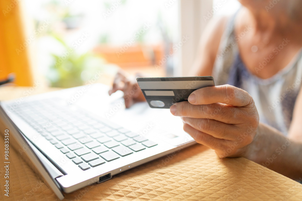 Elderly woman holding a credit card while using a laptop Elderly woman holding a credit card while using a laptop