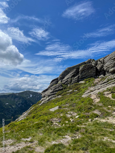 Moss-Covered Rocks Against a Backdrop of Mountains and a Blue Sky with White Clouds