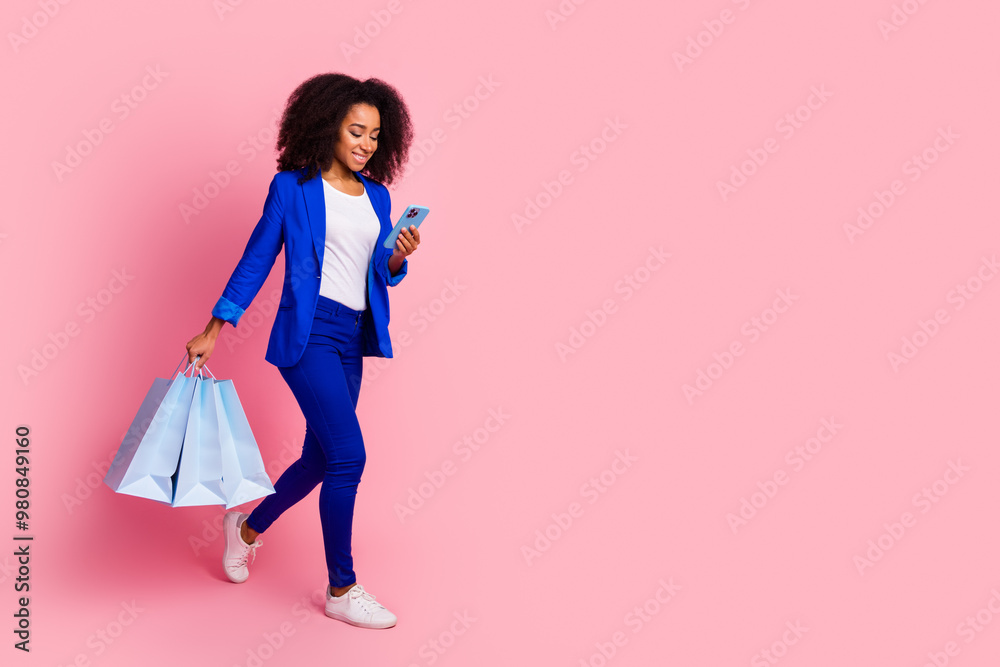 Full size photo of smart girl dressed blue jacket hold shopping bags look at smartphone go empty space isolated on pink color background Full size photo of smart girl dressed blue jacket hold shopping bags look at smartphone go empty space isolated on pink color background