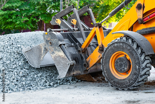 A yellow tractor with front hydraulic buckets rakes gravel at a construction site.