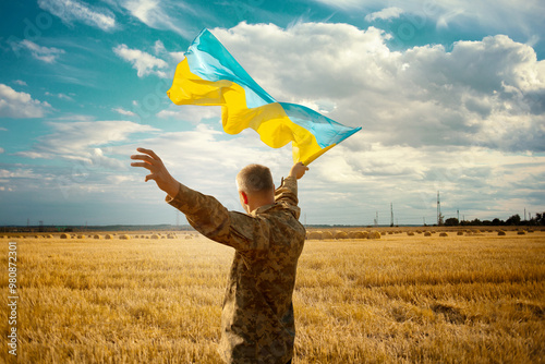 Incredibly beautiful picture as a symbol of freedom and independence of Ukraine. A soldier with a waving flag in a field in the rays of the sun