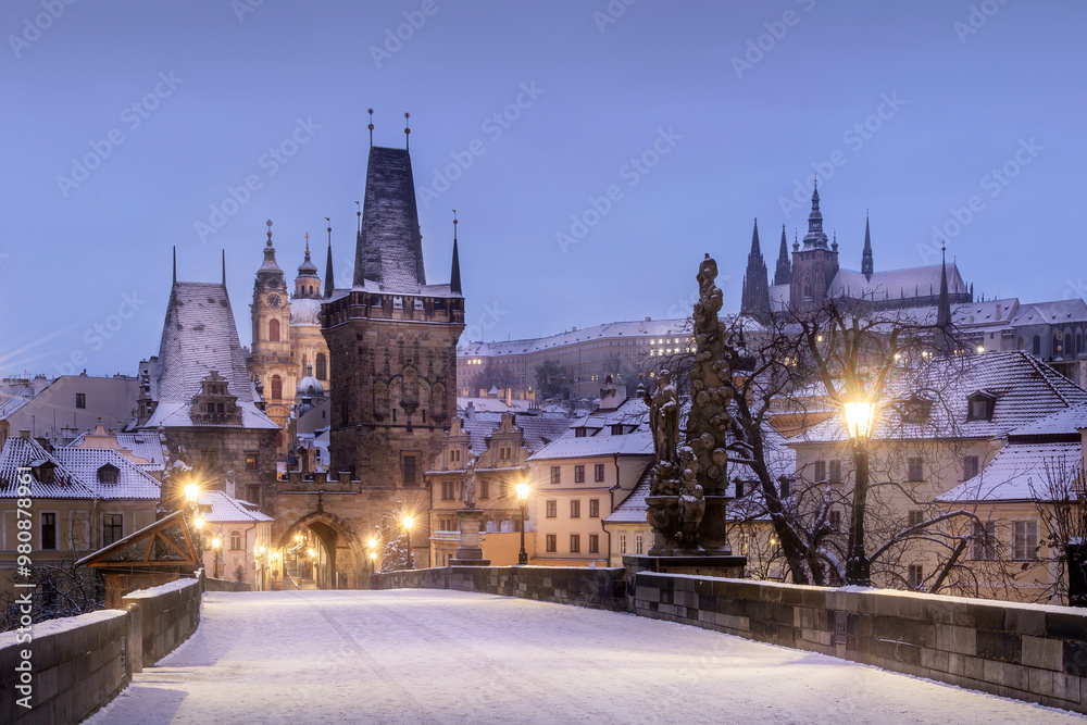 Naklejka premium View of Lesser town tower of Charles Bridge with Prague Castle in the background in Prague during in the early morning in winter under the snow. Czech Republic.