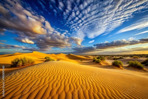 Golden sandy dunes stretch towards the horizon, wispy clouds scattered across a bright blue sky, in a serene