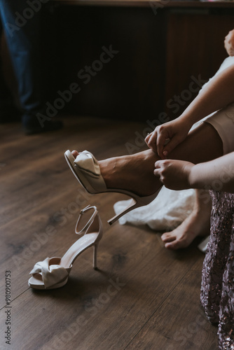 Mujer pone zapato de novia a novia antes de la boda, vemos vestido blanco nupcial