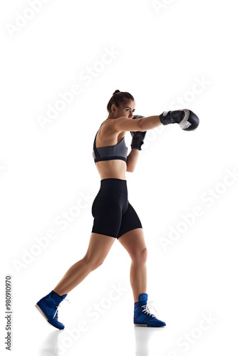 Full-length image of concentrated young girl with athletic body, pressing boxing, jab punch technique, isolated on white studio background. Concept of sport, hobby, active and healthy lifestyle