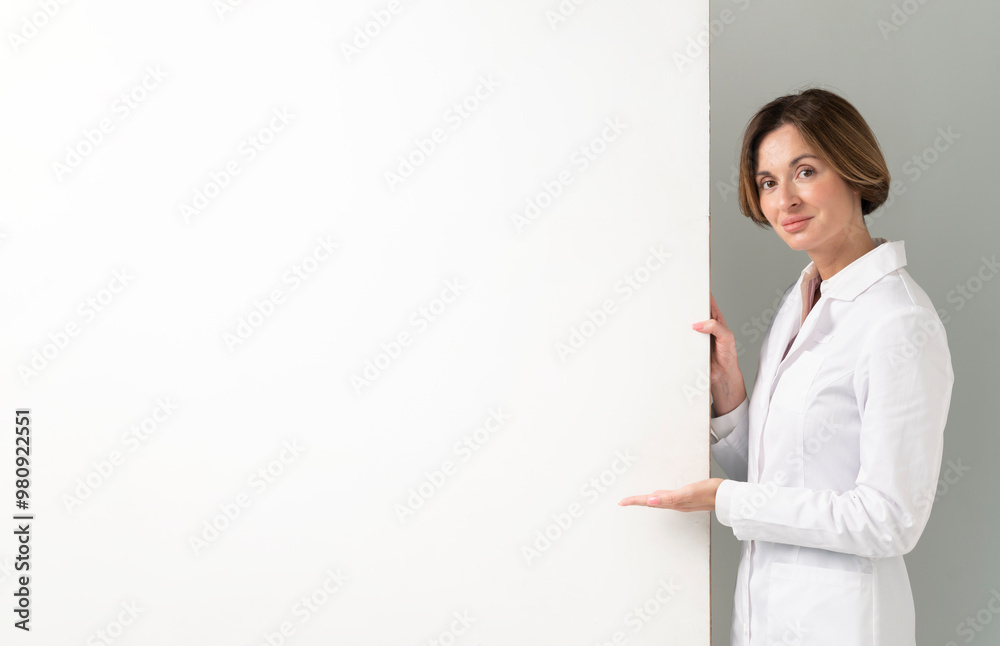 Female doctor standing and pointing on blank banner isolated on white background Female doctor standing and pointing on blank banner isolated on white background