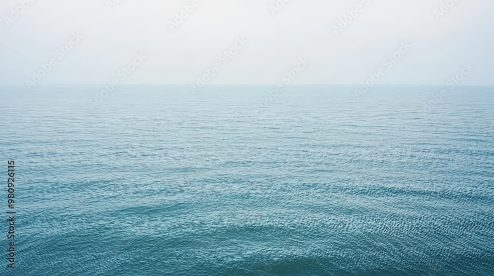 Obraz premium Tranquil blue ocean water with a soft, misty sky above.