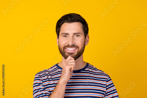 Photo of good mood clever man with stylish beard dressed striped shirt hold hand on chin smiling isolated on yellow color background