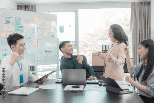 A diverse group of business professionals gather at a conference table in an office to celebrate a business victory, a good sales result, and achieving a financial goal.