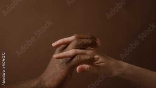 Close up view of hands of unrecognisable Caucasian woman and Black man reaching to each other and slowly connecting in lock on solid brown background