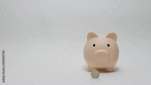 Coin dropping beside pink piggy bank on clean white background illustrates themes of savings, finance, and investment, emphasizing significance of financial planning