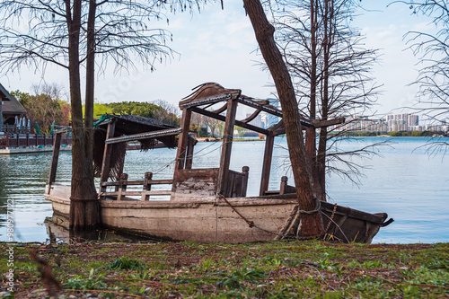 Abandoned wooden boat on shoreline of tranquil lake surrounded by trees and urban landscape photo