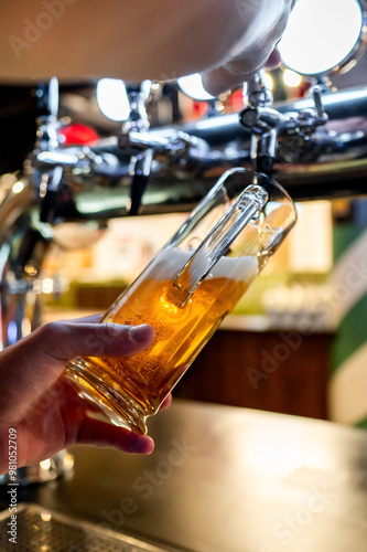 Close-up of a hand pouring beer from a tap into a glass at a bar. The background is blurred, highlighting the action and the golden color of the beer. Perfect for themes of hospitality, nightlife