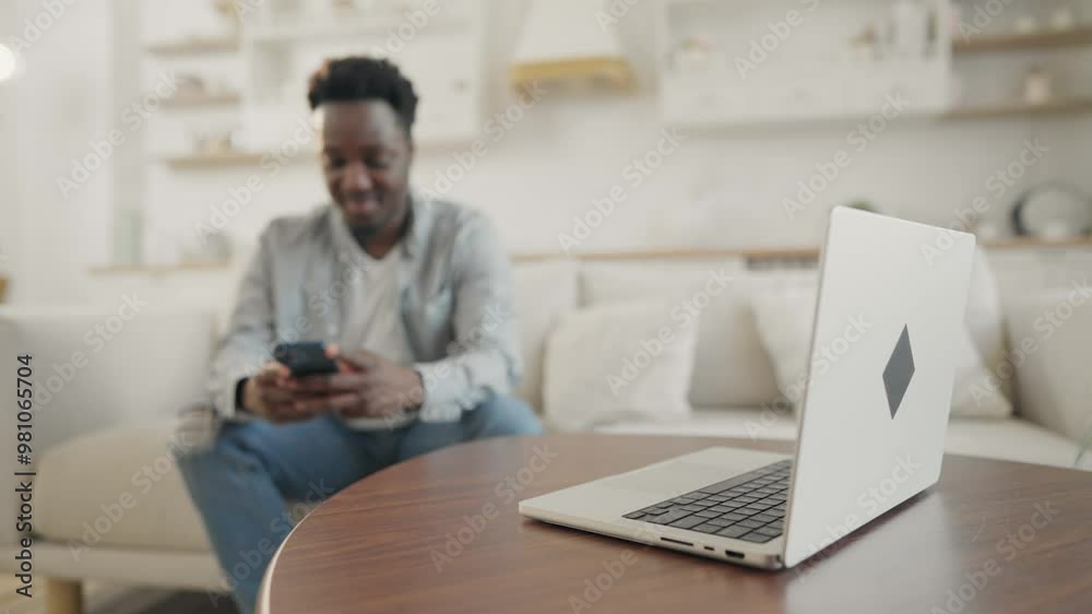 Modern people and gadgets, young black man with smartphone at home, open laptop . Freelancer or student in living room, internet addiction, overuse of social media and mobile devices, PC on table Modern people and gadgets, young black man with smartphone at home, open laptop . Freelancer or student in living room, internet addiction, overuse of social media and mobile devices, PC on table