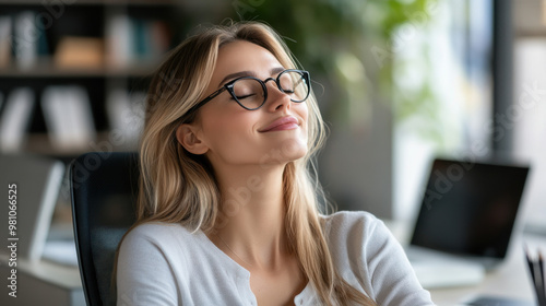 A serene woman in glasses takes a relaxing break in the office, highlighting work-life balance and mindfulness.