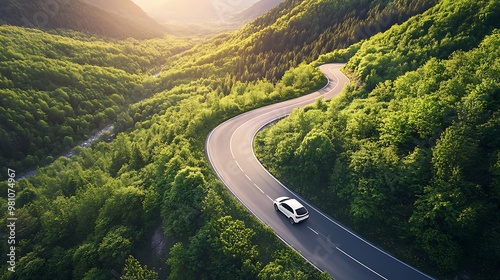 A car drives along a winding road through a lush green valley at sunset.