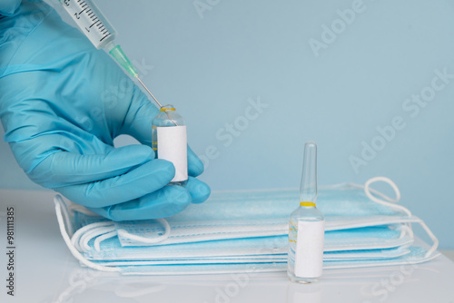 Mahing covid 16 vaccine injection, hands in medical gloves with vaccine ampoulas, copy space on blue background photo