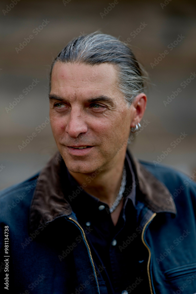 Mature man with grey hair and a leather jacket looks contemplatively to the side against a blurred background. Mature man with grey hair and a leather jacket looks contemplatively to the side against a blurred background.