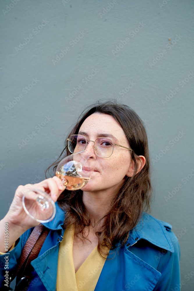 Woman in blue coat sipping white wine against a grey background. Woman in blue coat sipping white wine against a grey background.