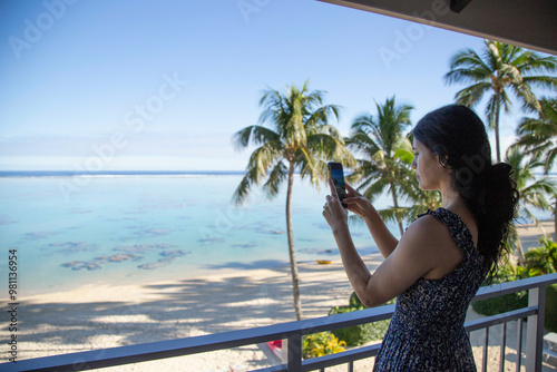 Woman takes a photo of a tropical beach view from a balcony with her smartphone, Titikaveka, Rarotonga, Cook Islands photo