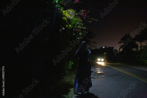 woman walking alone at night with oncoming vehicle headlights, Titikaveka, Rarotonga, Cook Islands photo