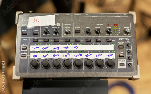 Audio mixing console with multiple adjustment knobs and channel inputs marked with handwritten labels. photo