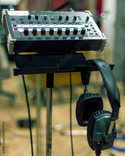Audio mixing console and headphones on a stand with blurred background in a recording studio.