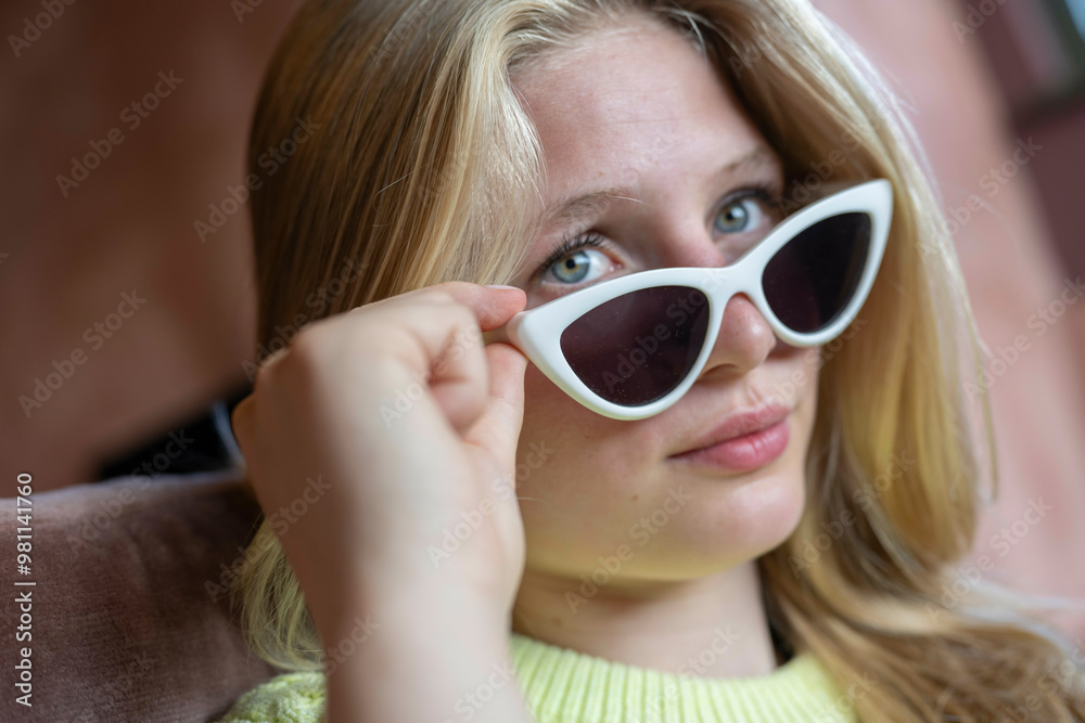 Young woman holding white sunglasses near her face with a thoughtful expression. Young woman holding white sunglasses near her face with a thoughtful expression.
