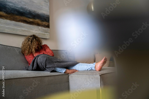 A person lounging comfortably on a gray sofa, barefoot, with a focus on relaxation and cozy home environment. photo