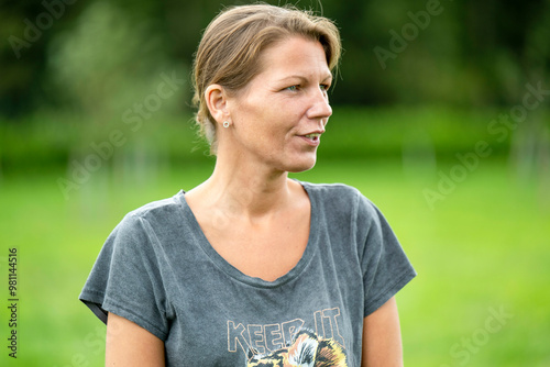 Woman standing outdoors with a thoughtful expression, wearing a casual grey t-shirt with a graphic print. photo