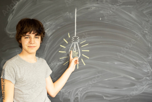 Tennage Boy thinking and getting an idea with empty black board in background photo