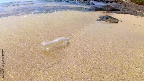 Ocean waves washed plastic bottle up on the shore. Disposable plastic waste pollutes the beach. Marine pollution caused by human. Poor trash management affects the environment.