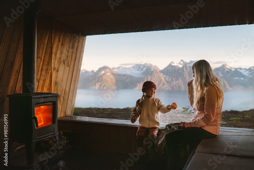 Foto Family mother and child relaxing in cozy mountain hut with fireplace and panoram