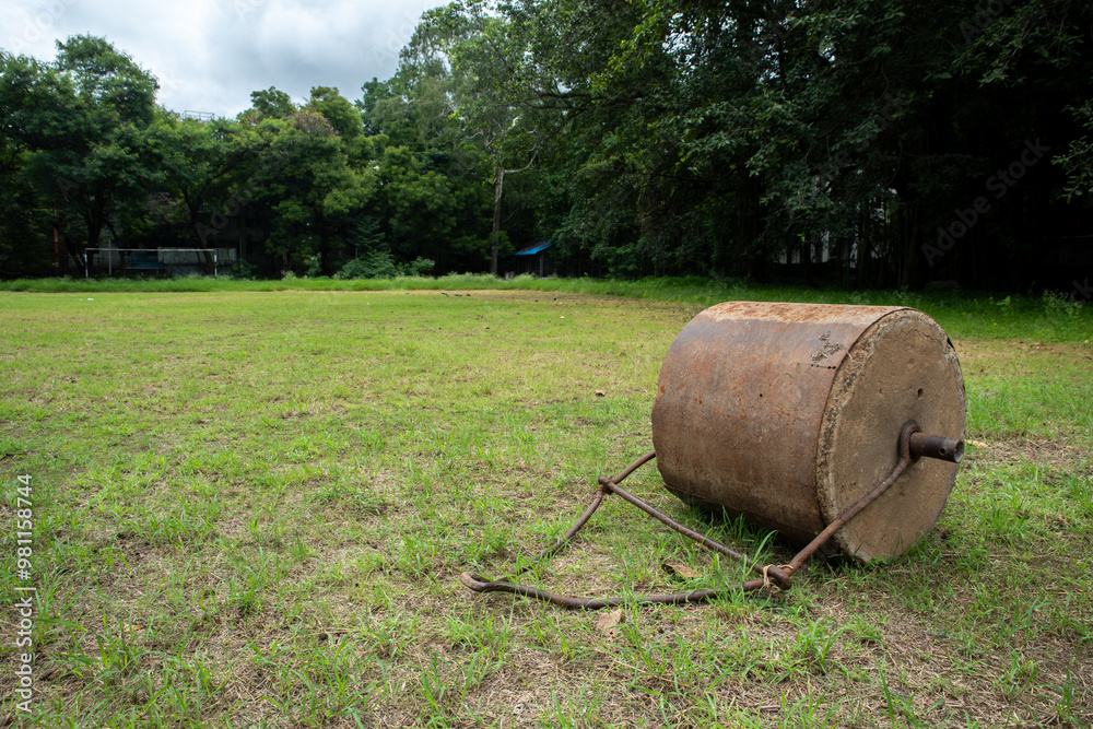 Soil roller laying of the field. Old rusty metal lawn roller on sports ground Soil roller laying of the field. Old rusty metal lawn roller on sports ground