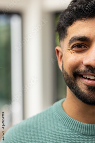 Smiling Indian man in green sweater enjoying time indoors, close-up portrait, copy space