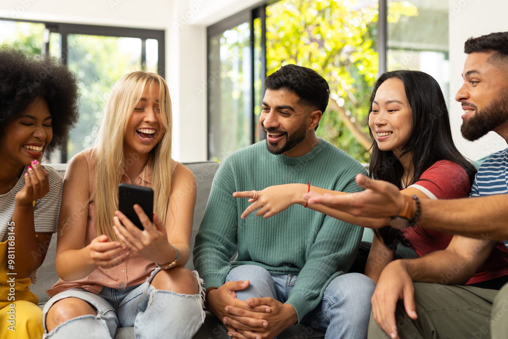 diverse friends sitting on couch, laughing and looking at smartphone together indoors diverse friends sitting on couch, laughing and looking at smartphone together indoors
