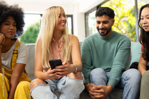 diverse friends sitting on couch, smiling and using smartphone, enjoying time together